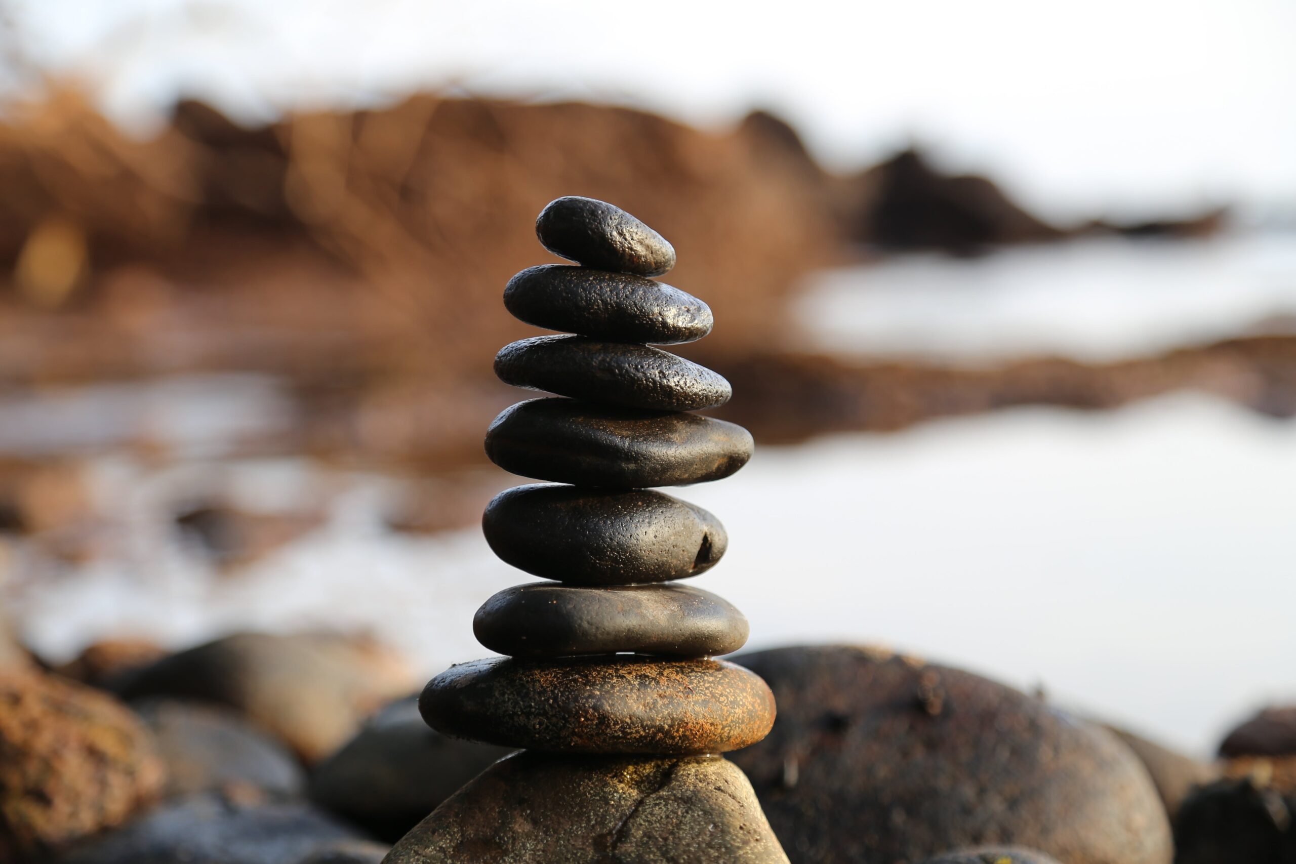 8 slightly flat round rocks balanced one above the other on a rocky shore with a blurred background,