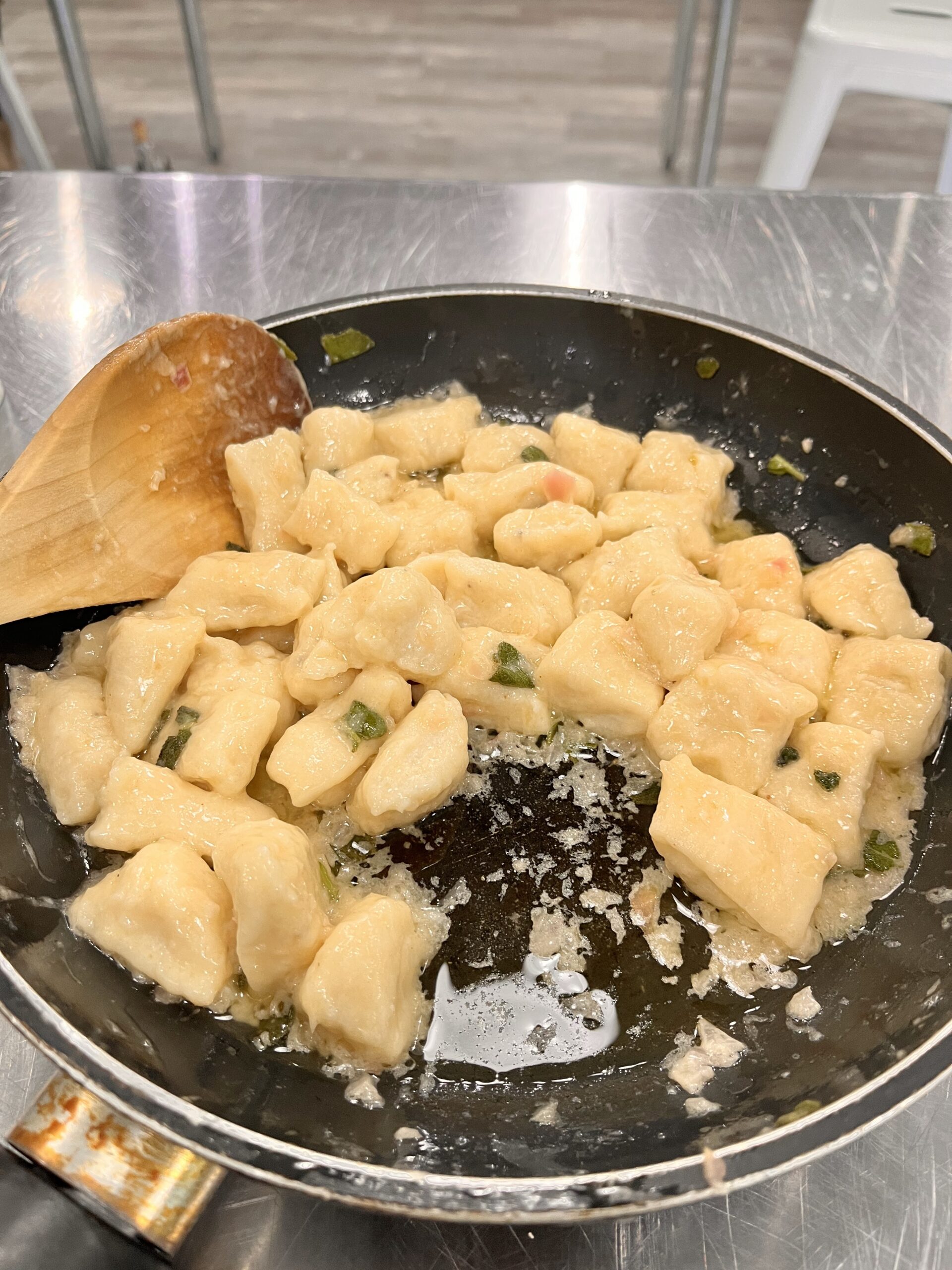 Bite size Gnocchi pasta dough ready for cooking in a pan with a wooden spoon for tossing.