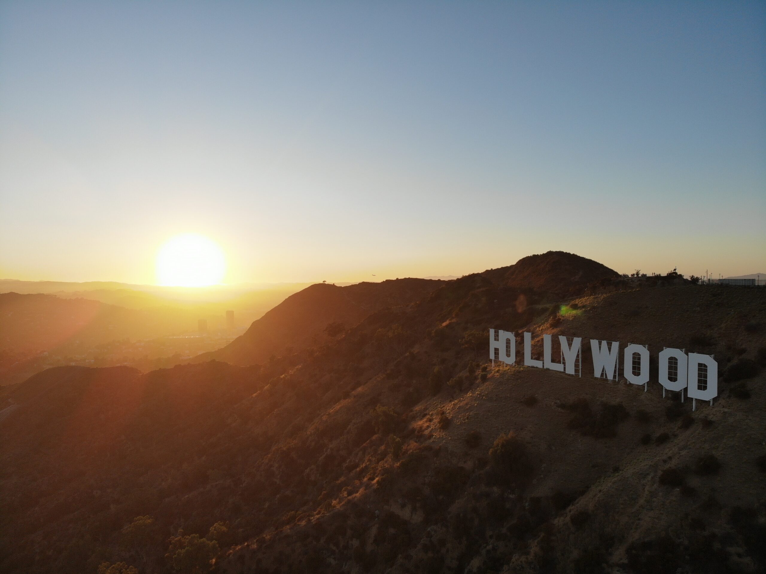 The white Hollywood sign sits atop a hill with a fading sun setting in the background.