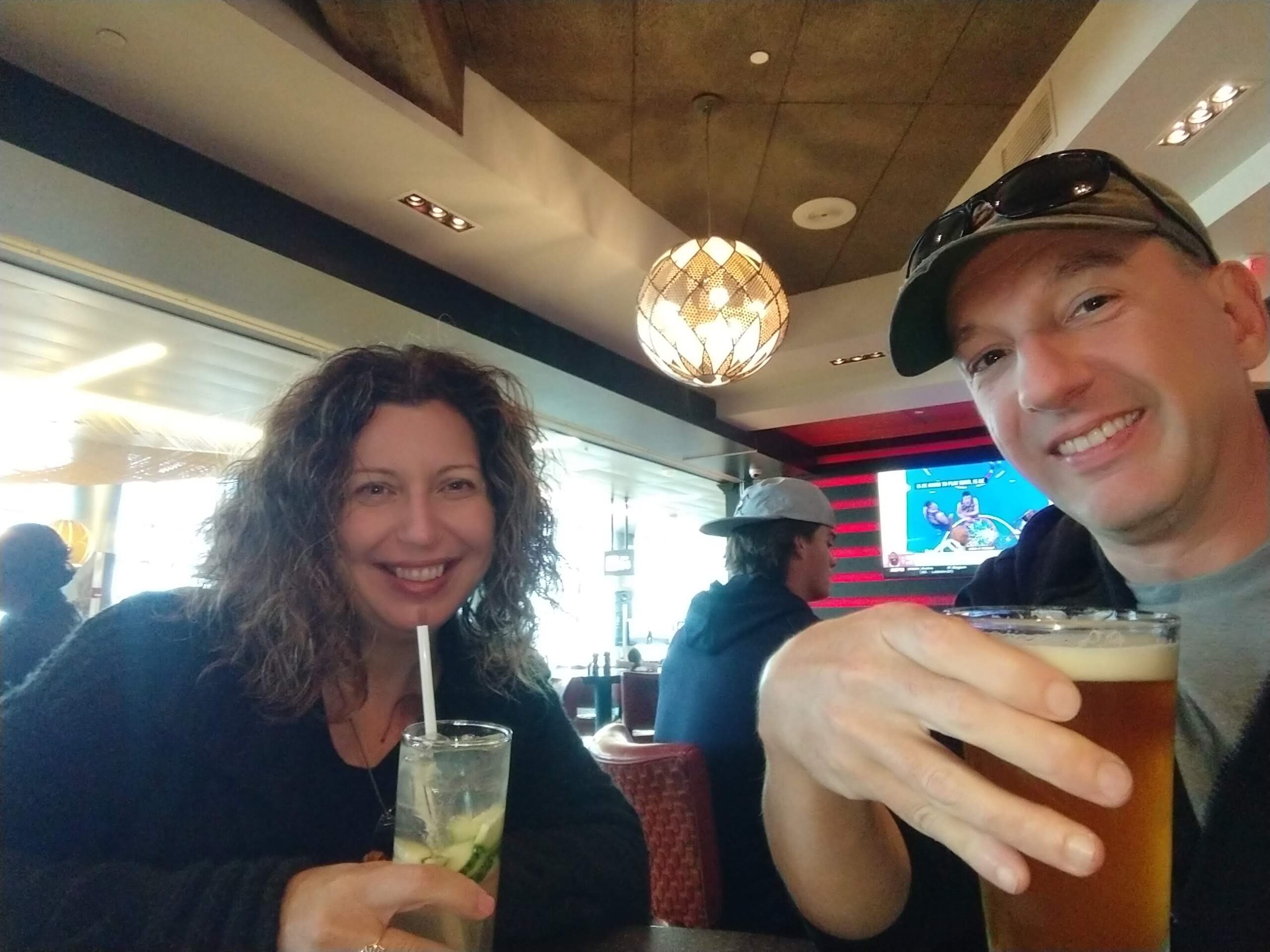 A woman and a man sitting next to each other at a bar are holding different types of cocktail while smiling.