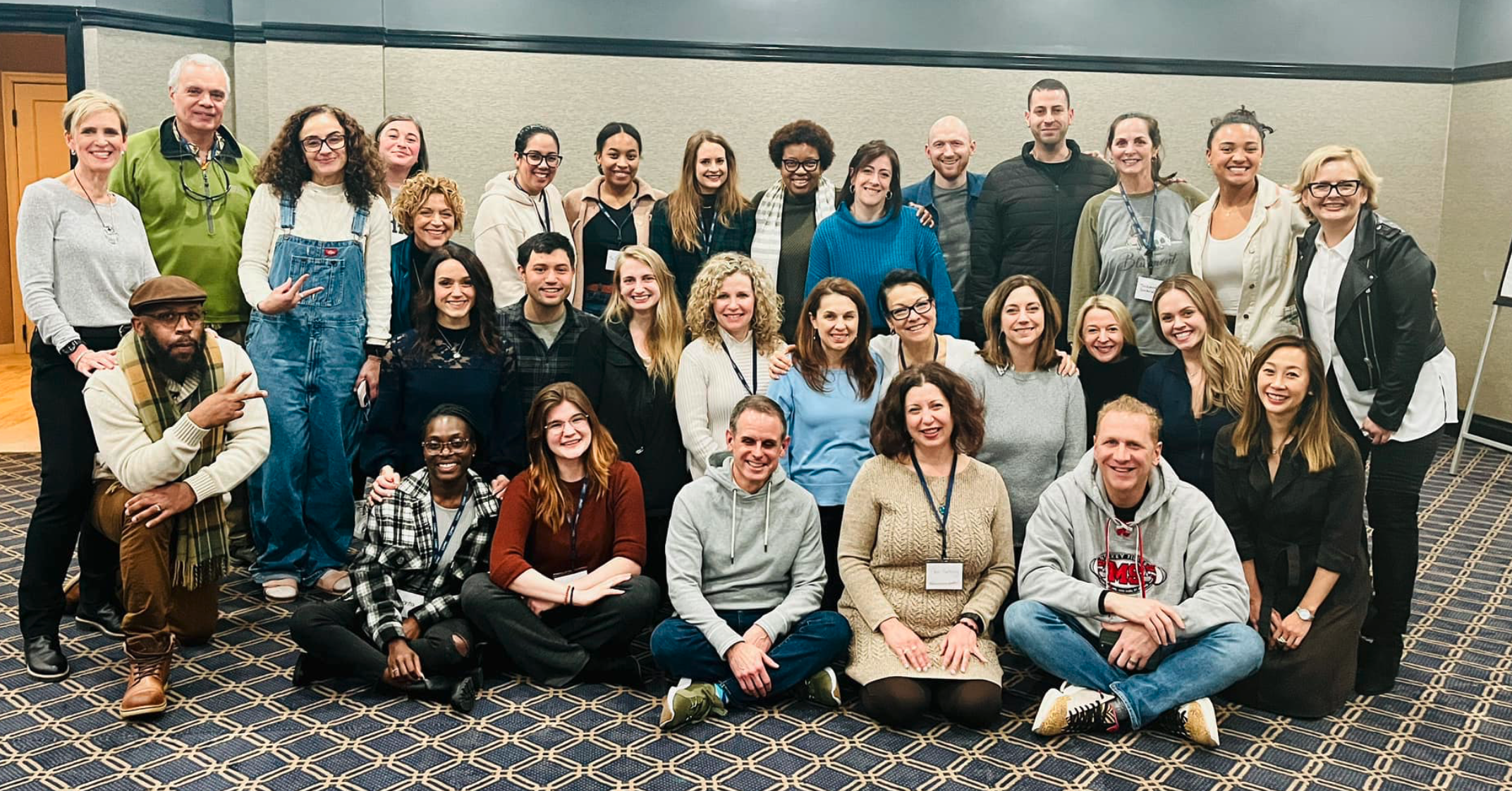 A cohort of male and female coaches gathered together at a conference lined up in three rows to capture their time together.