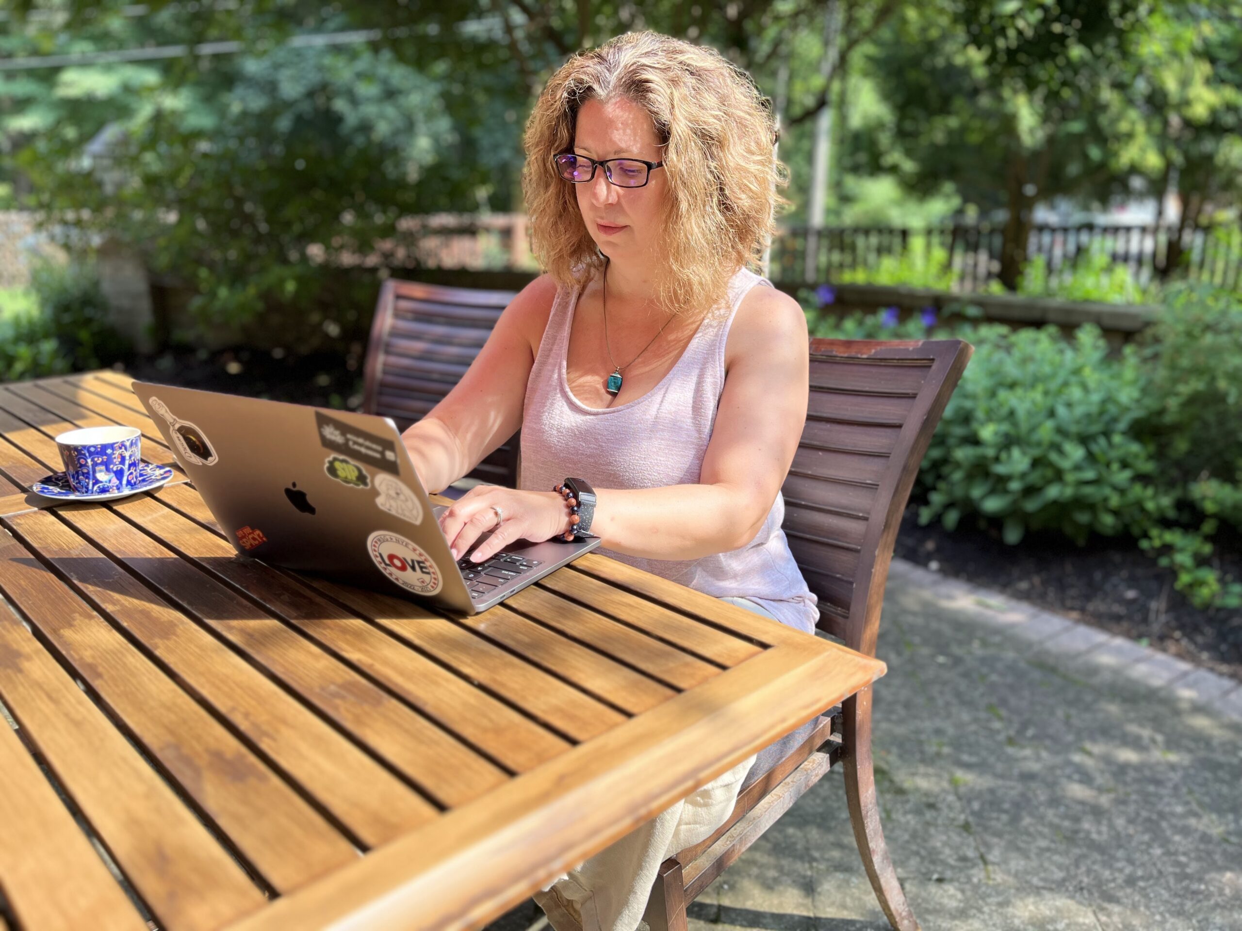 A woman peacefully typing on her laptop which sits on a table in her backyard.