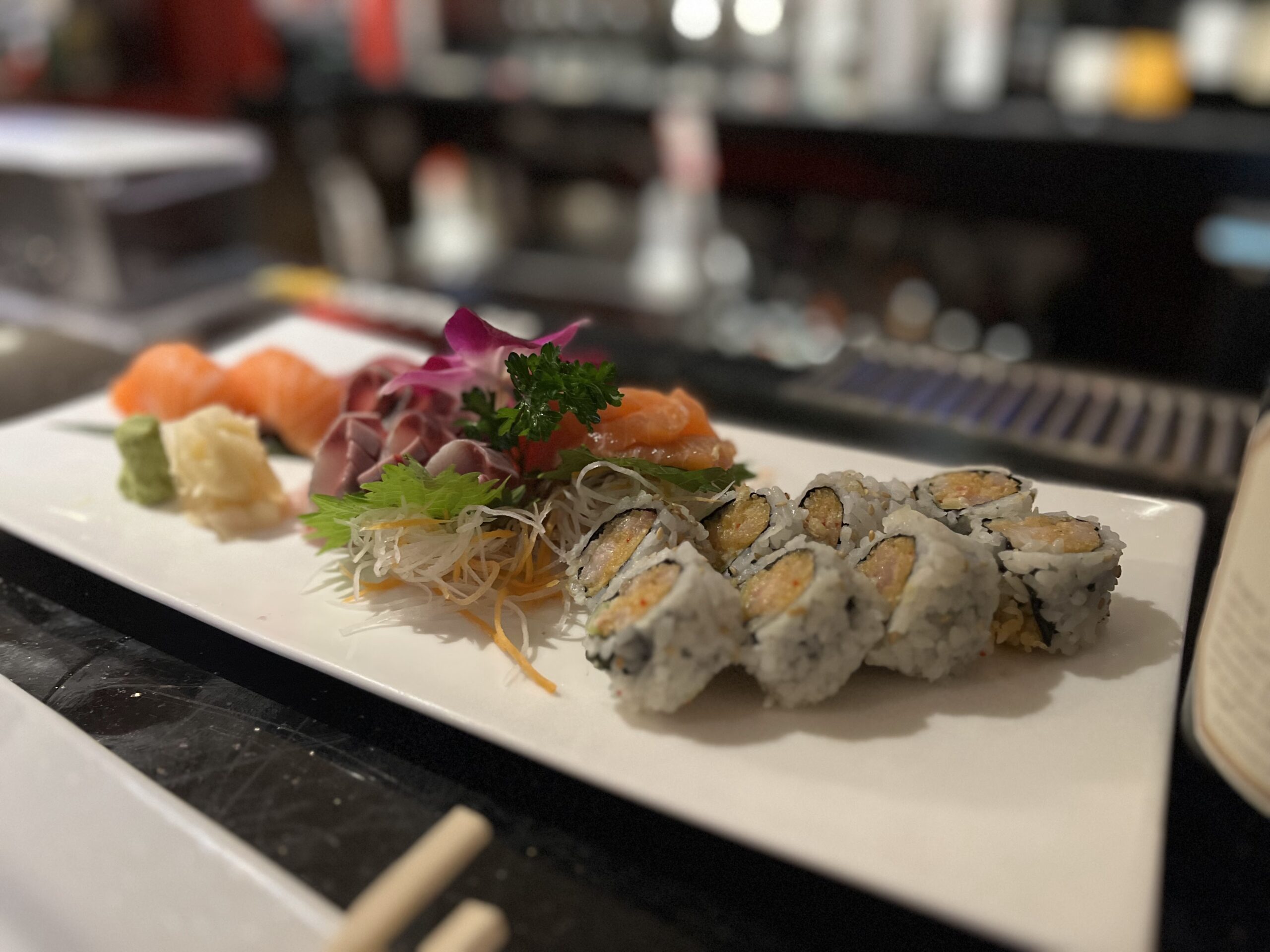 A white plate is filled with two chopped rolls of sushi paired with other colorful vegetables.