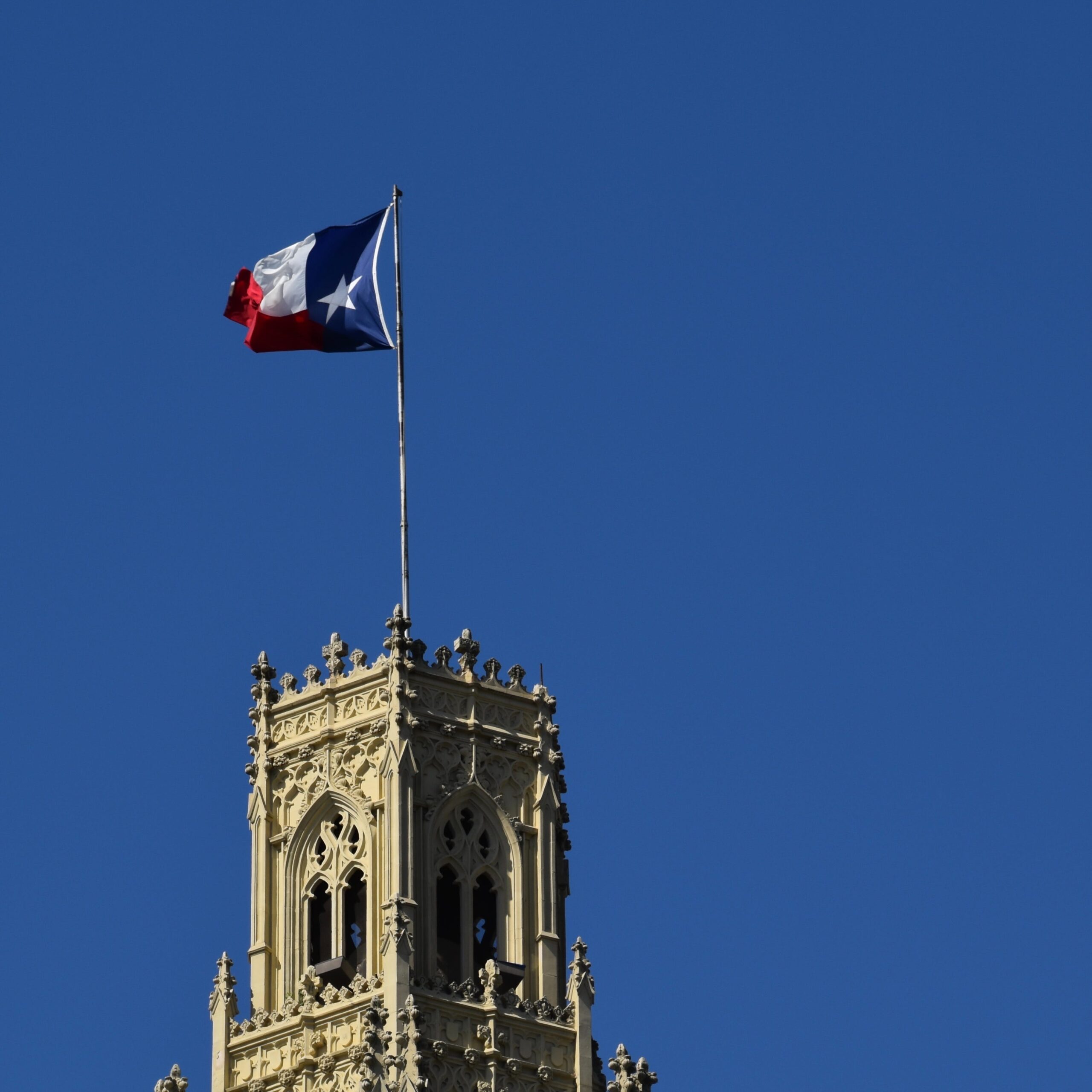 Flag of Texas atop a tan colored ornate building with a very blue sky in the background.