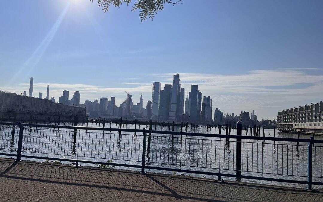 The skyline of Hoboken, NJ seen over a body of water on a partially cloudy day, with mostly blue skies.